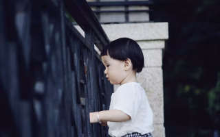 Young child standing quietly by a metal fence