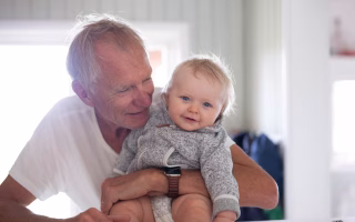 Smiling grandfather holding a happy baby indoors.