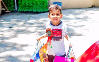 Smiling young boy holding colorful gift bags at a birthday party.