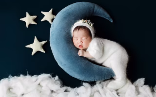 Sleeping baby curled on a moon pillow with stars and clouds