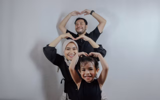 Smiling family posing together and making heart shapes with their arms.