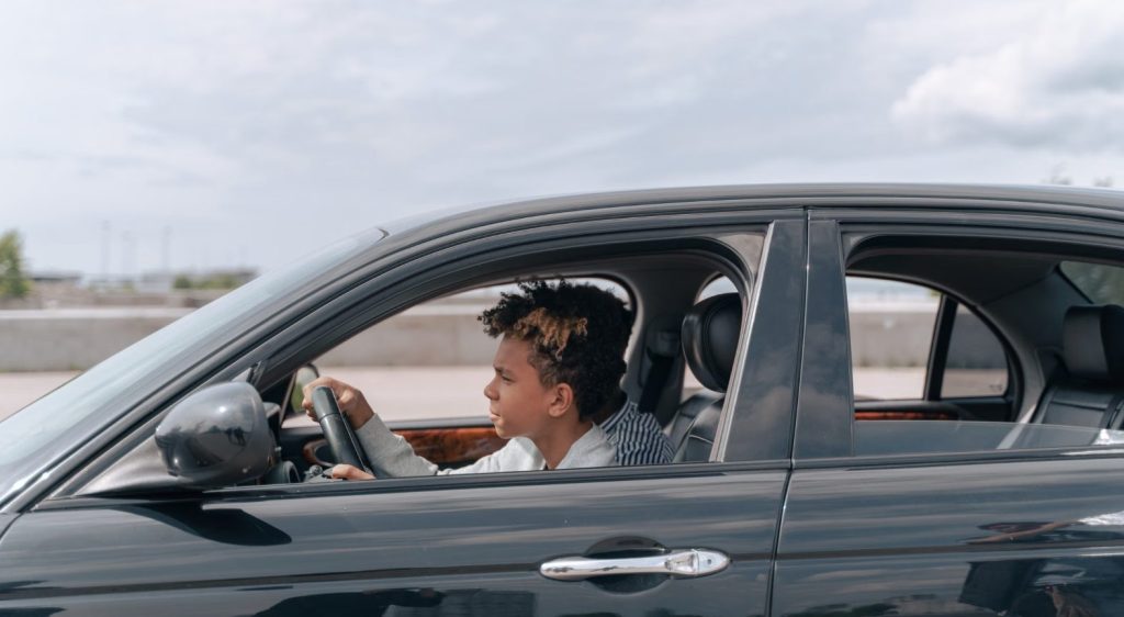 Teenage boy sitting in the driver's seat of a dark gray car
